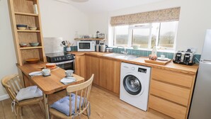 A compact kitchen with wooden cabinets, a built-in oven, a microwave, a washing machine, and a window with a view of the countryside. - The Wash House (Banbury)