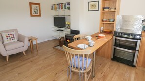 A modern kitchen with a wooden dining table, a built-in oven, and a television. - The Wash House (Banbury)