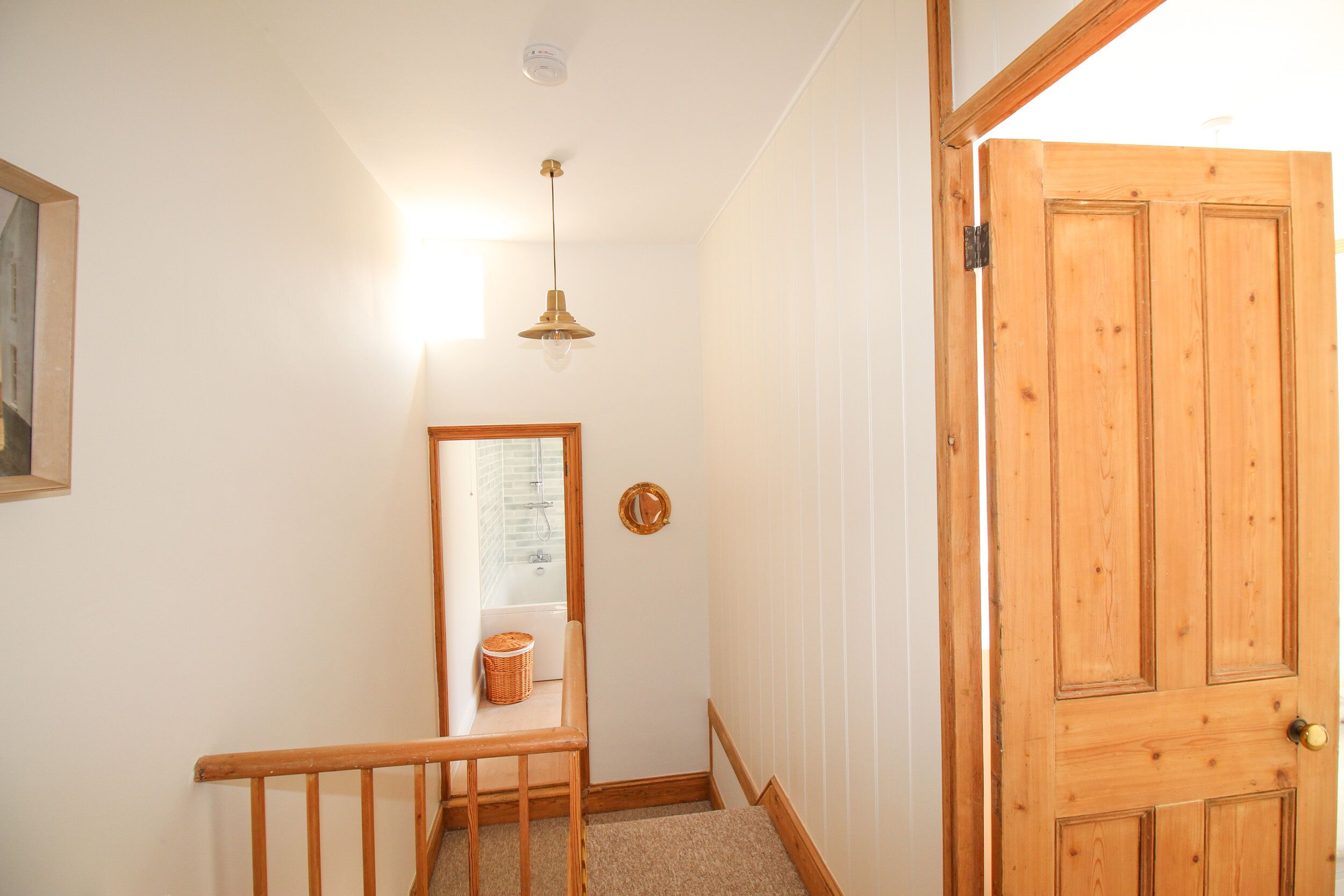 A hallway with a wooden door, a small table with a basket, a hanging light fixture, and a framed picture on the wall.
