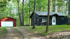 A rustic cabin with a red garage and a black main building, surrounded by a forested area.