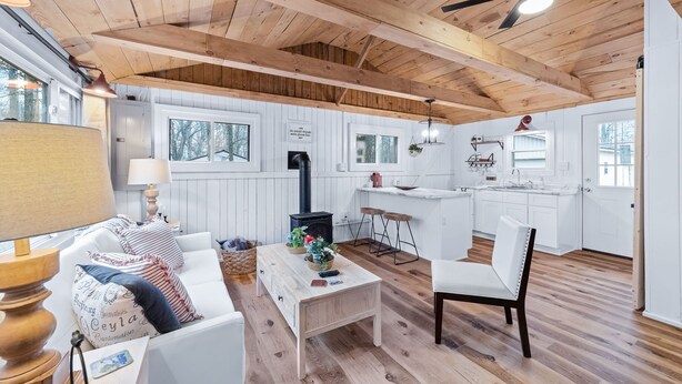 A cozy cabin interior with a wooden ceiling, a fireplace, a dining area, and a kitchen.