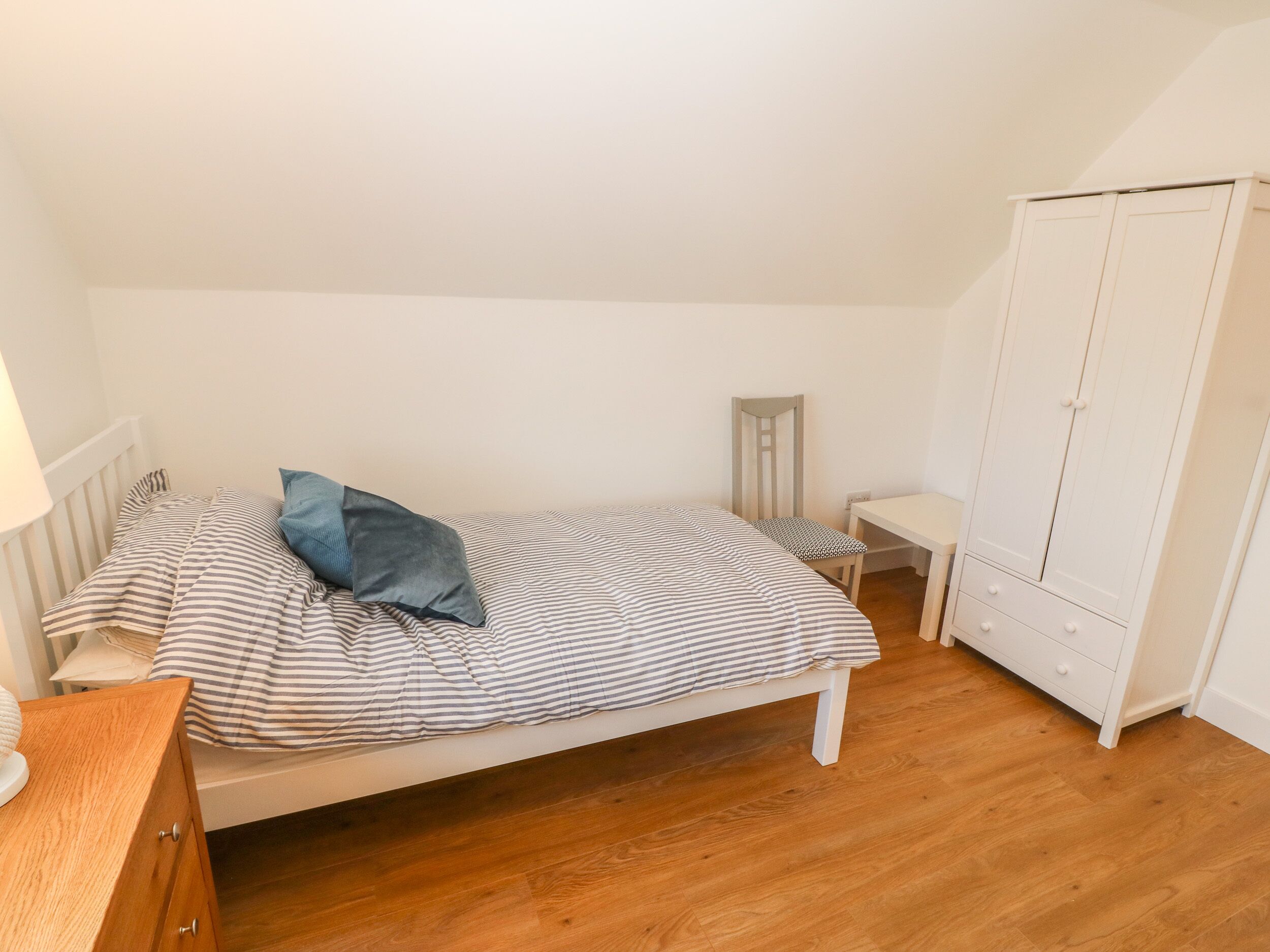 A bedroom with a bed, a small table, a chair, a wardrobe, and a lamp.