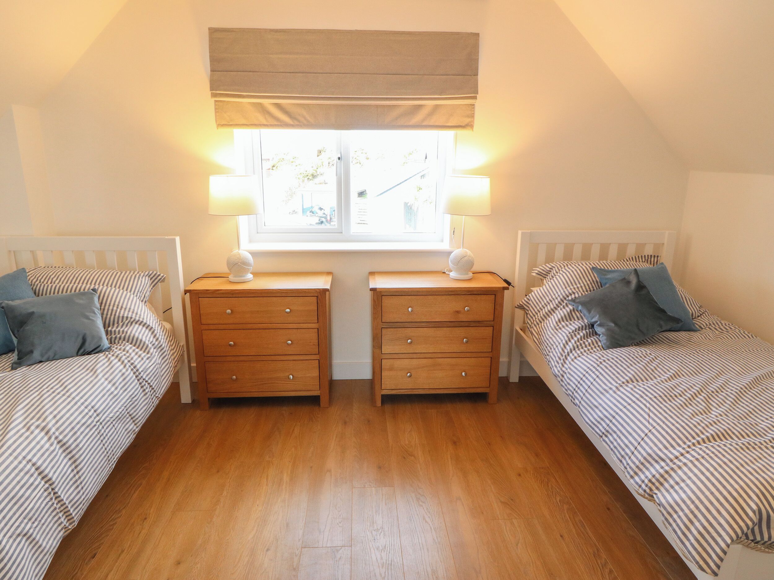 A bedroom with two single beds, wooden nightstands, and a window with a view.
