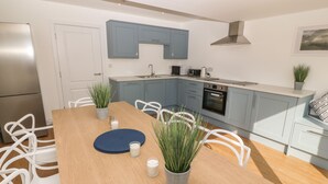 Cozinha moderna com armários azul-claros, geladeira de aço inoxidável e forno embutido. Há uma mesa de jantar com cadeiras brancas e plantas em vasos.