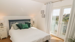 Quarto com cama, mesas de cabeceira, luminária, janela com cortinas e vista para o exterior.
