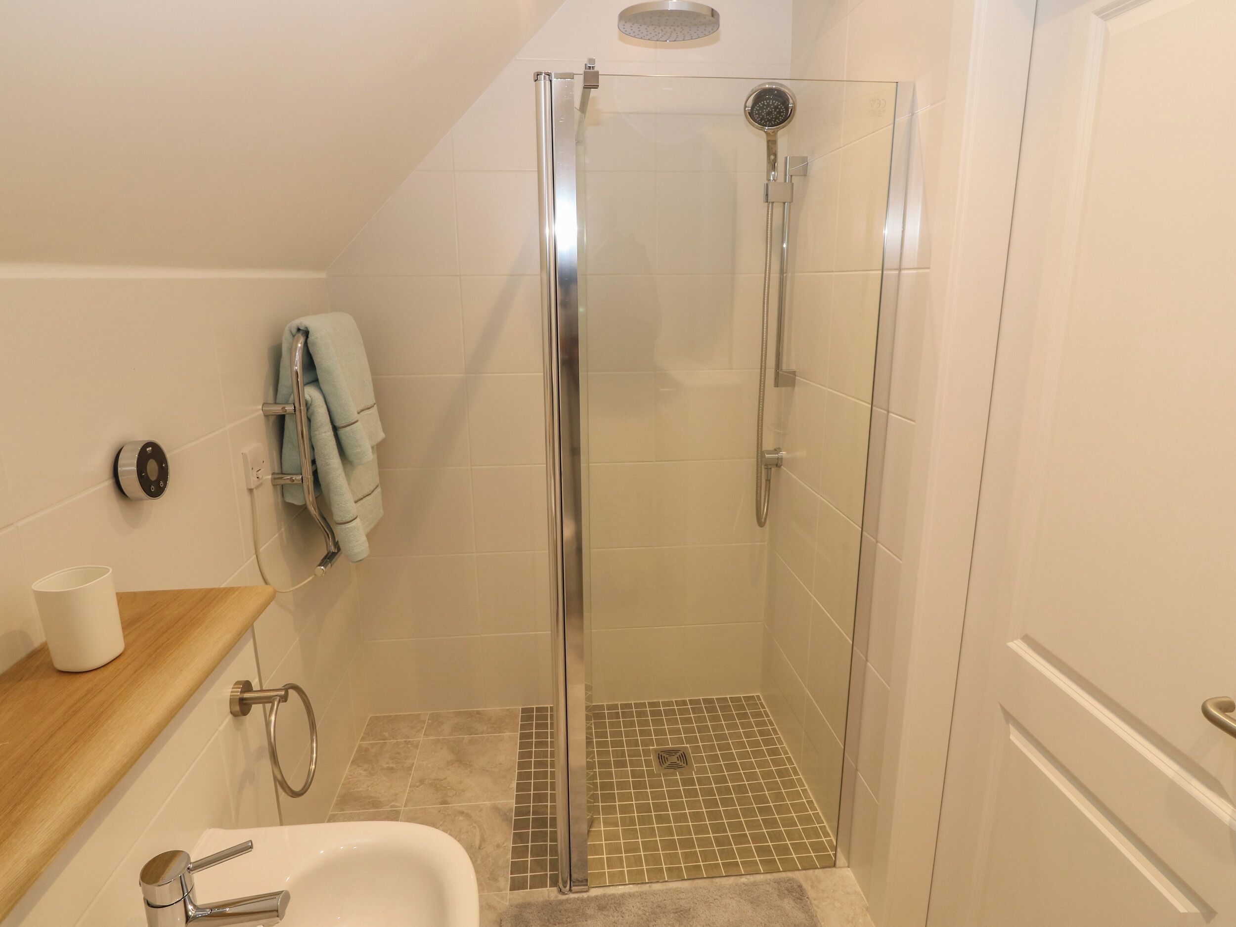 Un baño moderno con ducha de vidrio, lavamanos blanco y perchero para toallas.