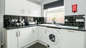 A modern kitchen with white cabinets, black countertops, and a built-in washing machine. - Rose Cottage (Skegness)