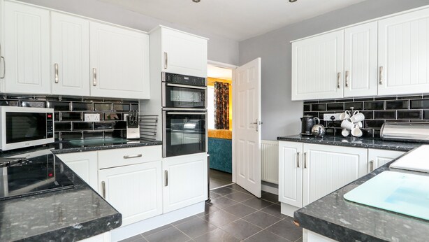 A modern kitchen with white cabinets, black countertops, a double oven, and a microwave. - Rose Cottage (Skegness)