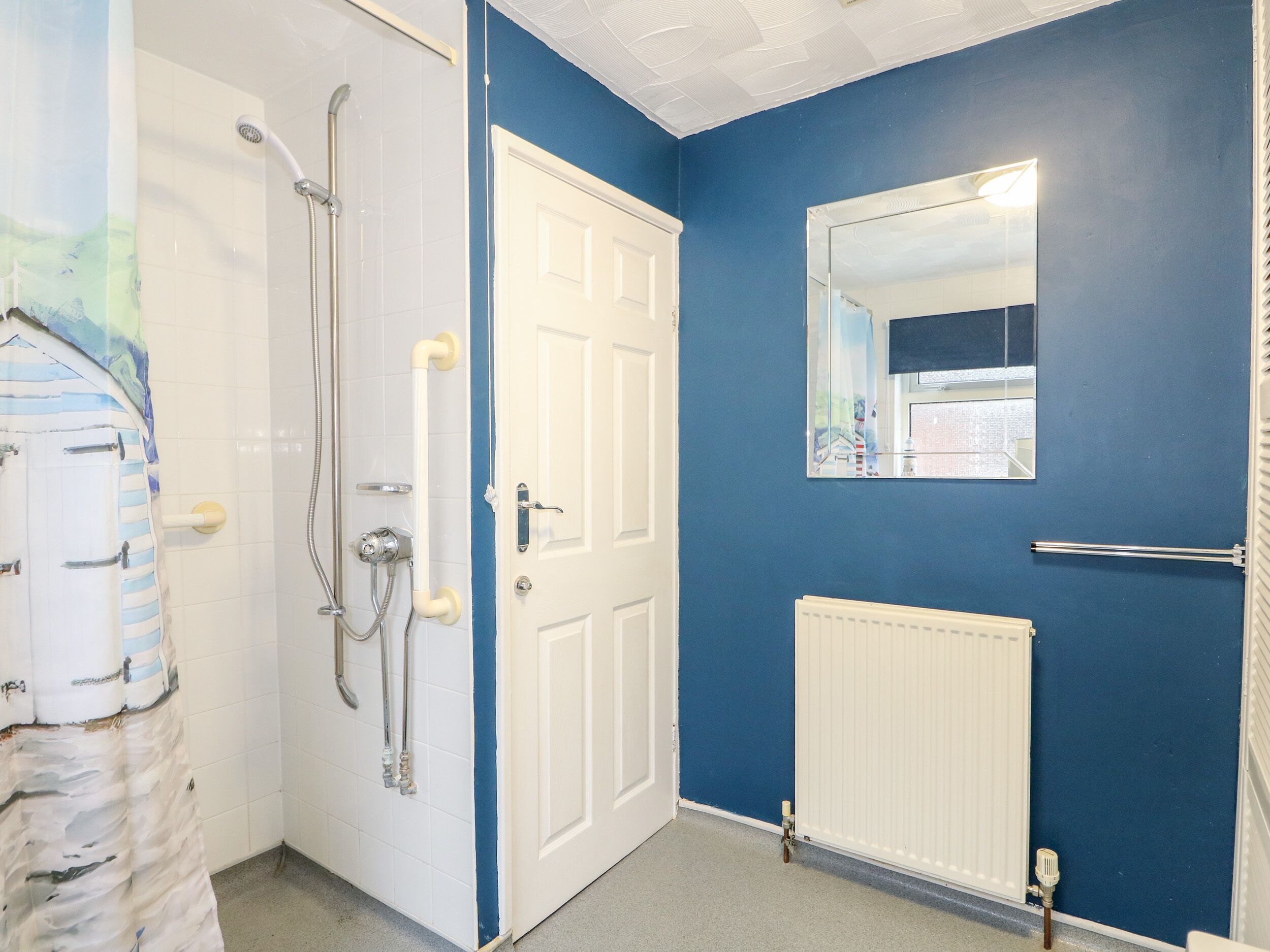 A bathroom with a white door, a blue wall, a mirror, and a shower with a hose.