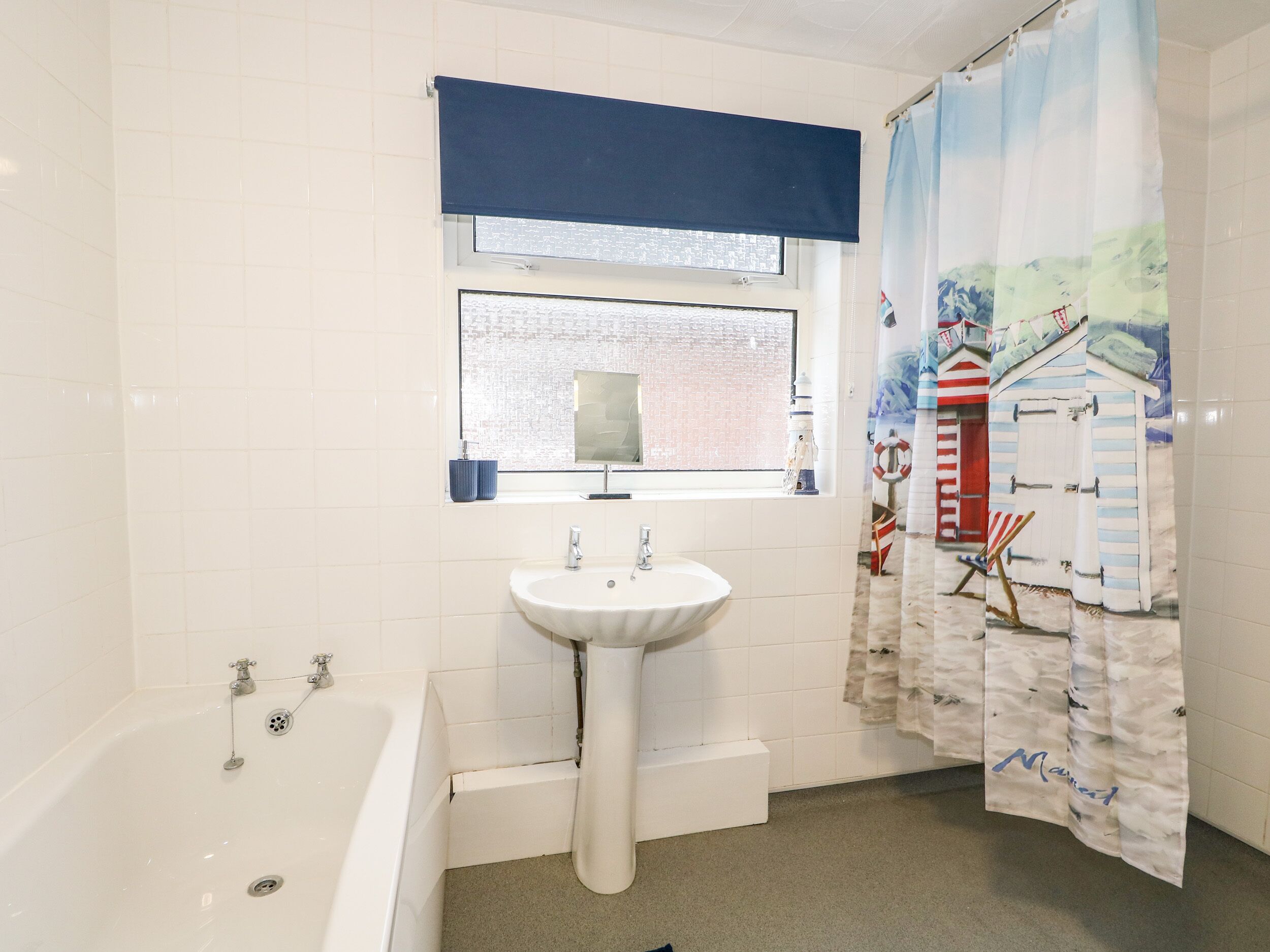 A bathroom with a white sink, a bathtub, a window with a view of a brick building, and a shower curtain with a nautical theme.