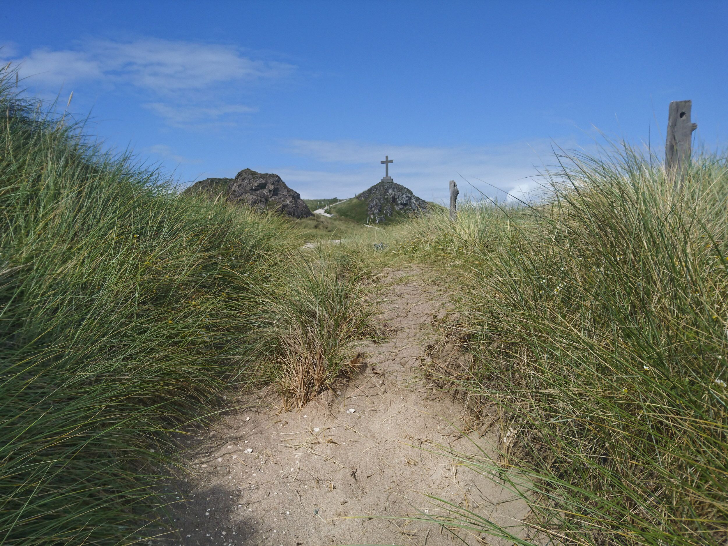 A dirt path leading to a rocky area with a cross monument.