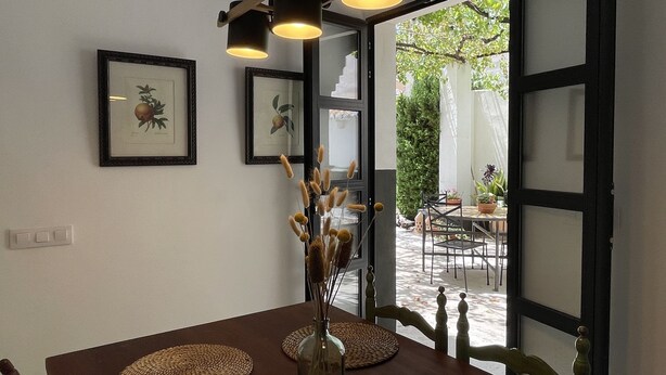 Un comedor con una mesa lista para dos comensales, una obra de arte enmarcada en la pared y vistas del jardín exterior a través de la puerta abierta.