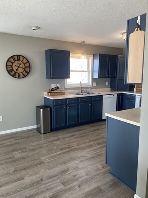 A modern kitchen with dark blue cabinets, a wooden clock, and a large window. - Summer rental on beautiful West Battle Lake! (Battle Lake)