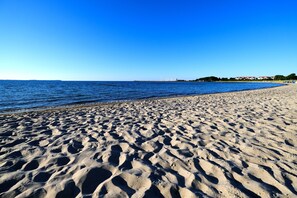 A sandy beach with clear blue water and a distant shoreline with buildings.