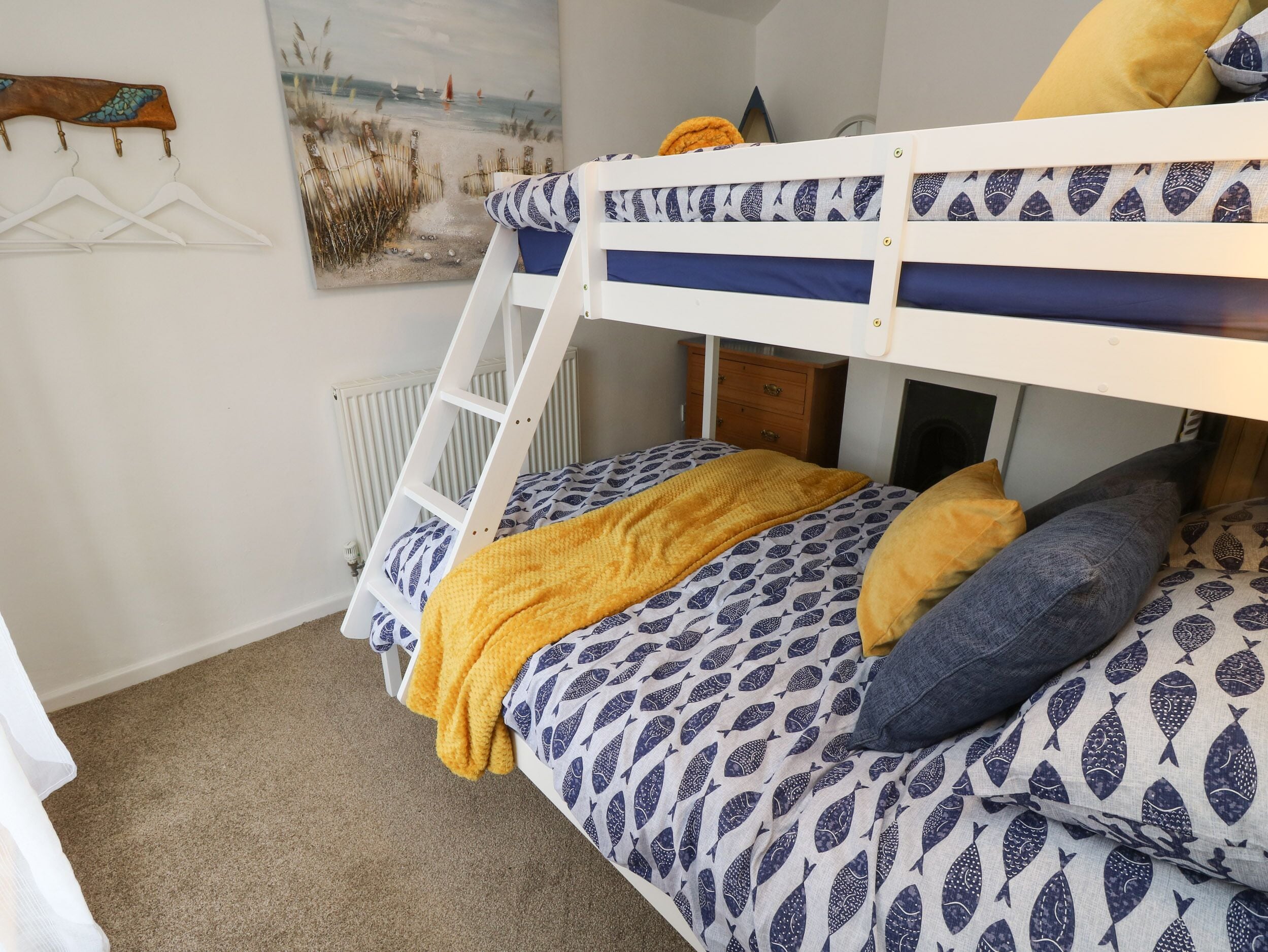 A bunk bed with a ladder, a wooden dresser, and a painting of a beach scene.