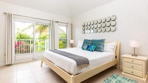A bedroom with a bed, bedside tables, a wall-mounted mirror, and a view of a balcony with plants. - Villa Stingray, Family-Sized Condo-5 minutes from the beautiful beach! (Providenciales)