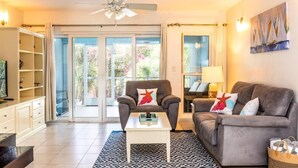 A living room with a sofa, armchair, and coffee table, a ceiling fan, and a sliding glass door leading to a balcony. - Villa Stingray, Family-Sized Condo-5 minutes from the beautiful beach! (Providenciales)