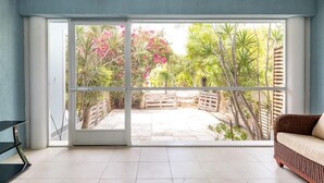 A room with a sliding glass door leading to a garden with tropical plants and a wooden fence. - Villa Stingray, Family-Sized Condo-5 minutes from the beautiful beach! (Providenciales)