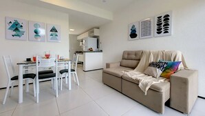 A modern living room with a beige sofa, a dining table with chairs, and abstract wall art. - Magnífica casa em Porto das Dunas (Aquiraz)