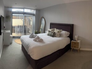 A bedroom with a bed, bedside table, and a view of the outside. - Fistral Apres Surf (Newquay)