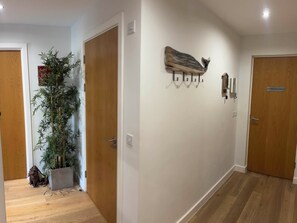 A hallway with wooden flooring, a potted plant, a wall-mounted cat decoration, and a door with a sign.