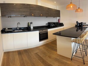A modern kitchen with a curved island, stainless steel appliances, and a built-in oven. - Fistral Apres Surf (Newquay)