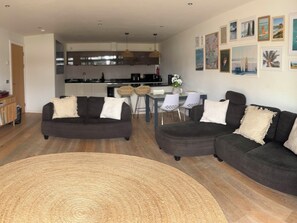 A modern living room with two dark sofas, a round woven rug, and a dining area with a table and chairs. - Fistral Apres Surf (Newquay)