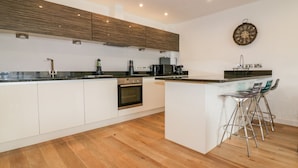 A modern kitchen with a central island, white cabinetry, and a wooden floor. - Fistral Apres Surf (Newquay)