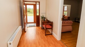 A hallway with a wooden floor, a radiator, a door leading outside, and a striped sofa with a red cushion. - Daisy's Cottage (Knockreagh)