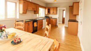 A spacious kitchen with wooden cabinets, a dining table with chairs, and a view to the outside. - Daisy's Cottage (Knockreagh)