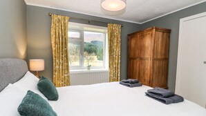 A bedroom with a large bed, two pillows, a nightstand with a lamp, a window with curtains, and a wooden wardrobe. - Ben Grianan (Aberfeldy)
