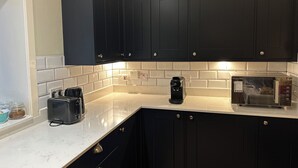 A modern kitchen with dark cabinets, a white countertop, a coffee maker, and a microwave. - Ben Grianan (Aberfeldy)