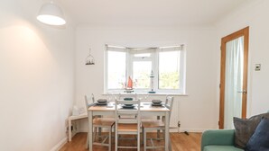 A dining area with a table set for four, a window with a view, and a green sofa. - Tillys Cottage (Weston-super-Mare)