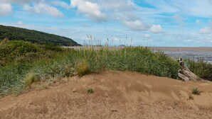 A coastal landscape with sand dunes, grassy vegetation, and a distant hill under a partly cloudy sky. - Tillys Cottage (Weston-super-Mare)