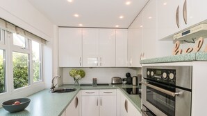 A modern kitchen with white cabinets, a green countertop, and stainless steel appliances. - Tillys Cottage (Weston-super-Mare)