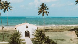 A white church with a cross on top, surrounded by palm trees and a sandy beach. - Pousada Haya (São Miguel dos Milagres)
