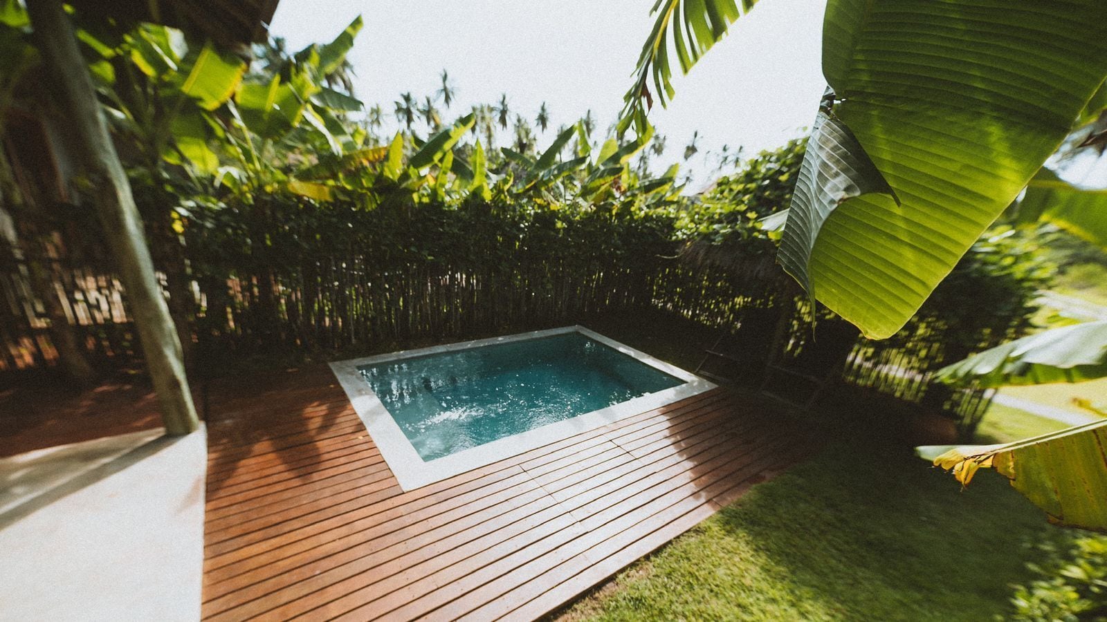 A rectangular hot tub on a wooden deck surrounded by lush greenery.