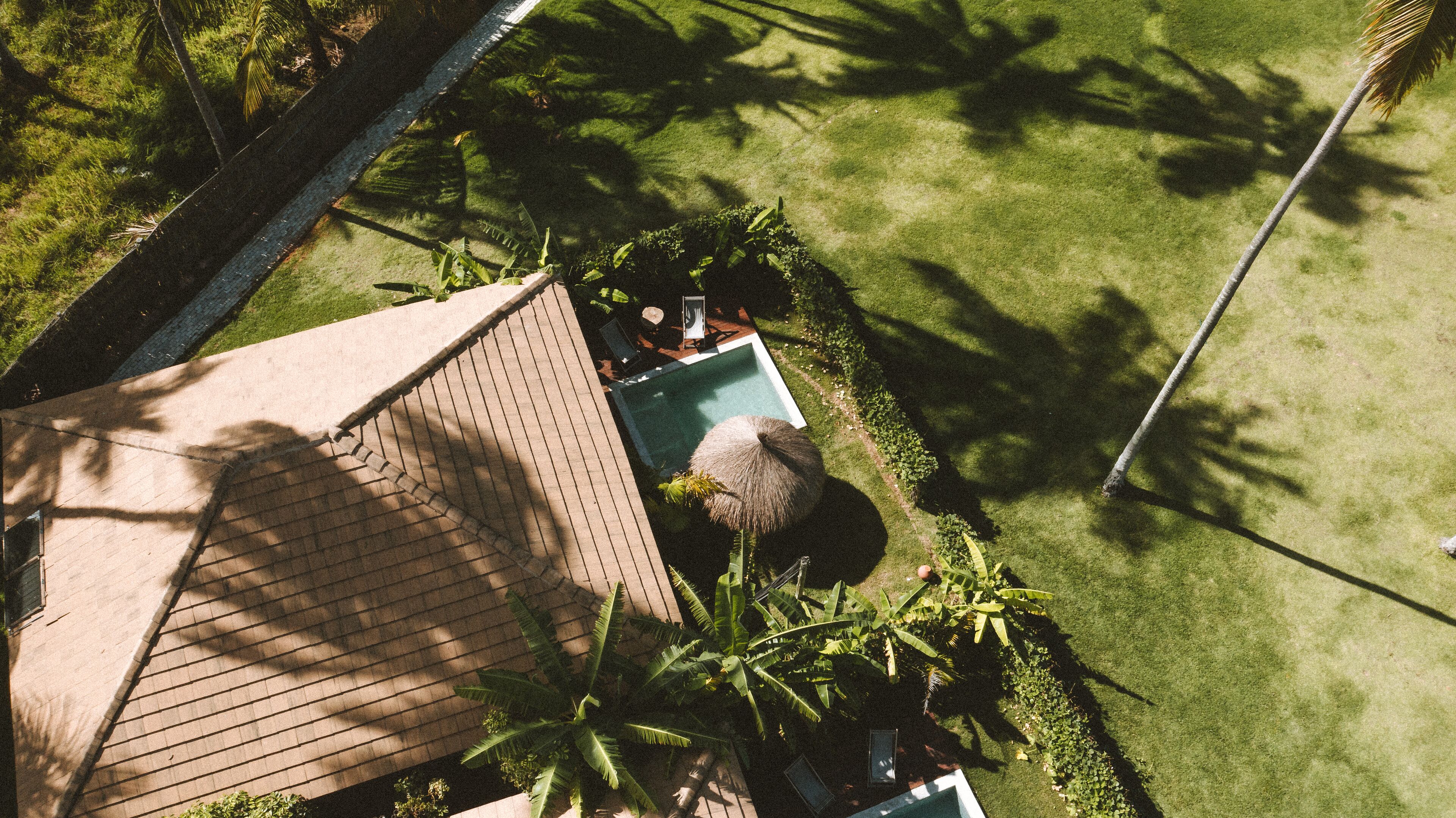 An aerial view of a residential property with a swimming pool, a thatched-roof structure, and lush greenery.