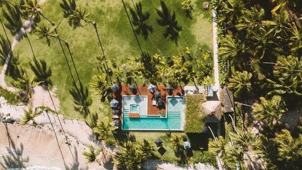 An aerial view of a beachfront property with a swimming pool, palm trees, and a beach area. - Pousada Haya (São Miguel dos Milagres)