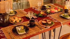 A dining table set with plates of food, glasses, and a wine rack in the background. - Pousada Haya (São Miguel dos Milagres)