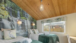 Quarto com duas camas, teto de madeira, janela com vista para uma cerca de madeira e um mural na parede retratando uma cascata.