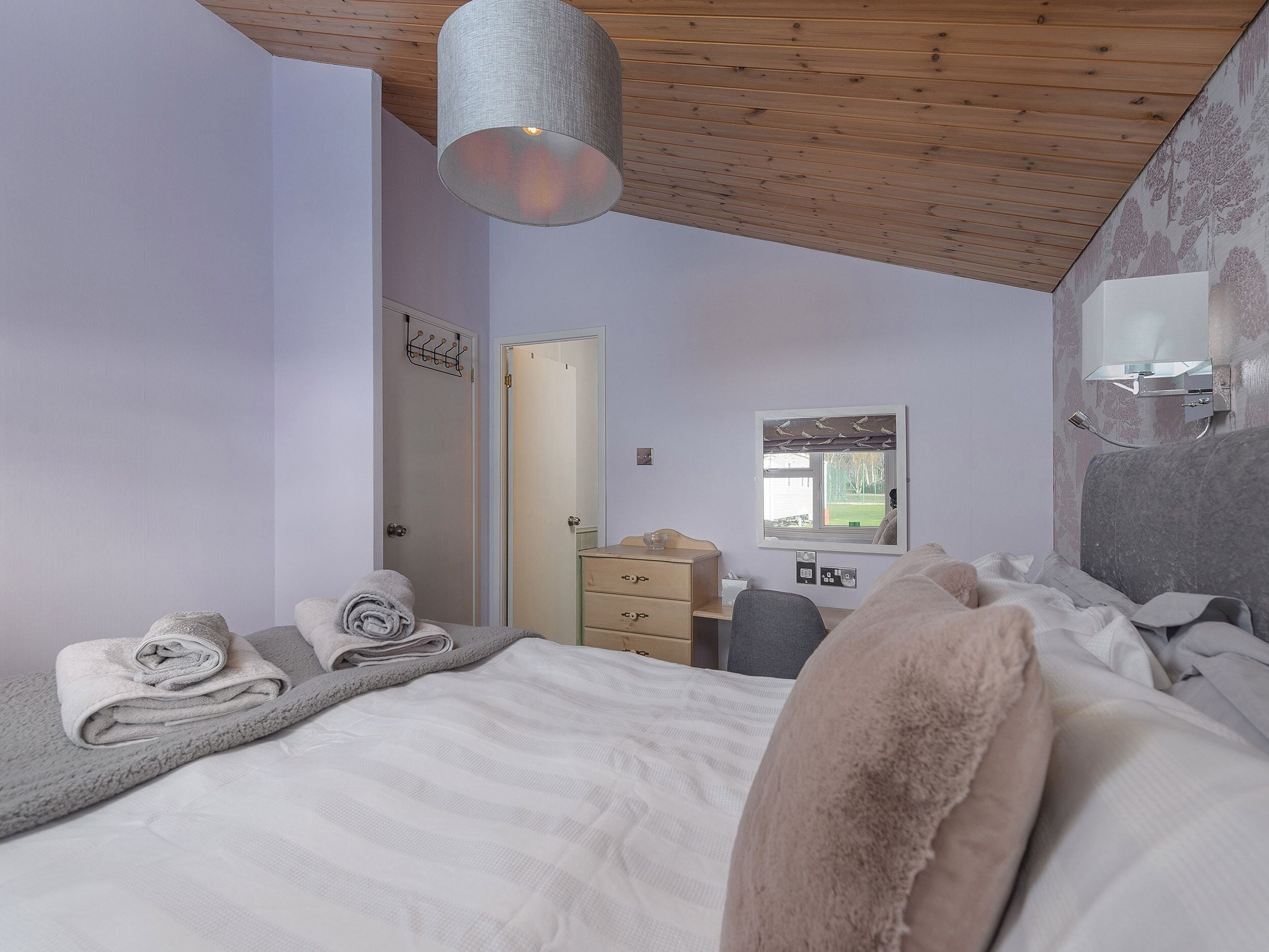 Une chambre à coucher avec un lit, un bureau, une chaise, un miroir et une fenêtre.