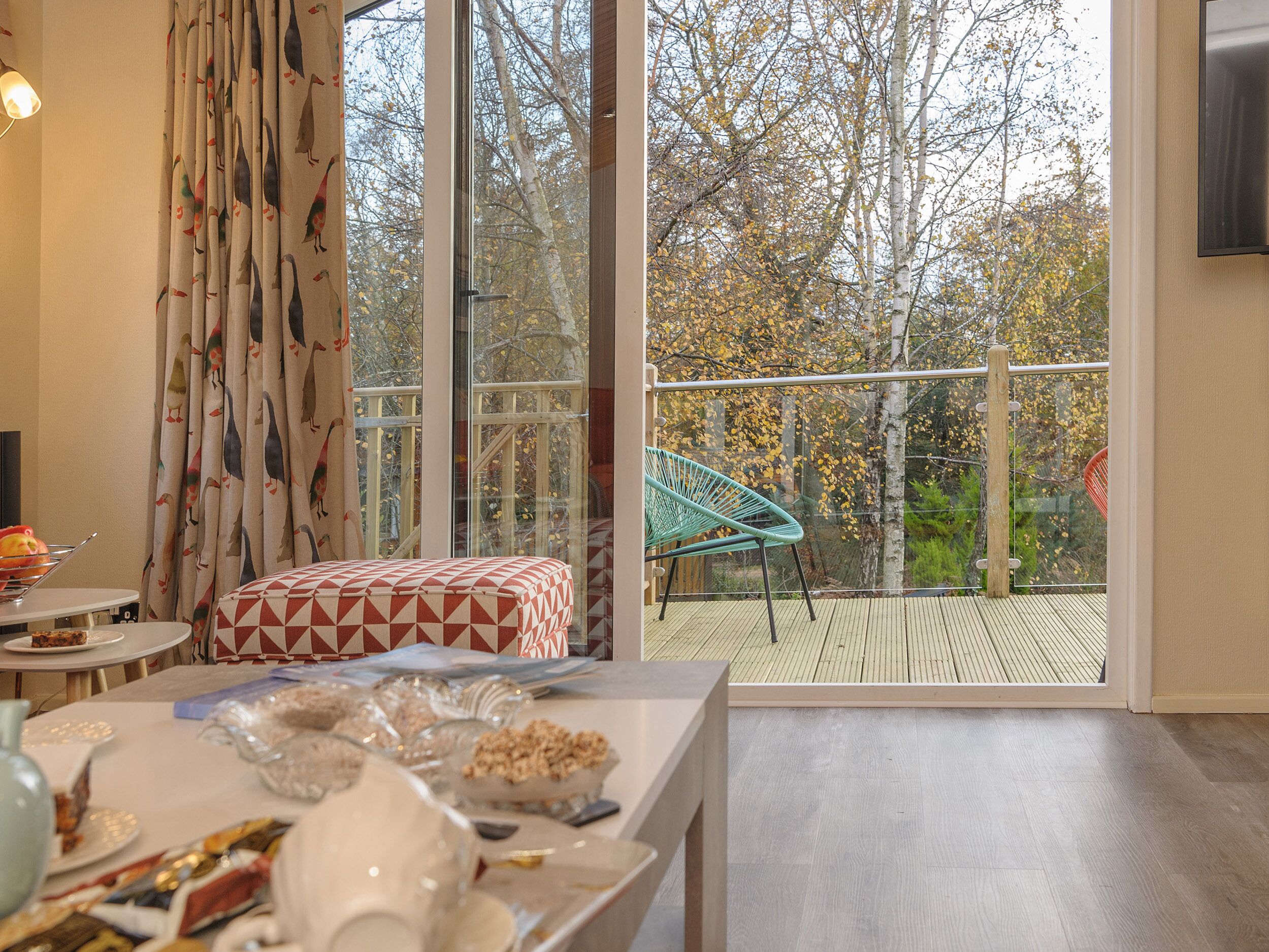 A dining area with a table set for a meal, a chair, and a view of the outdoors through large windows.