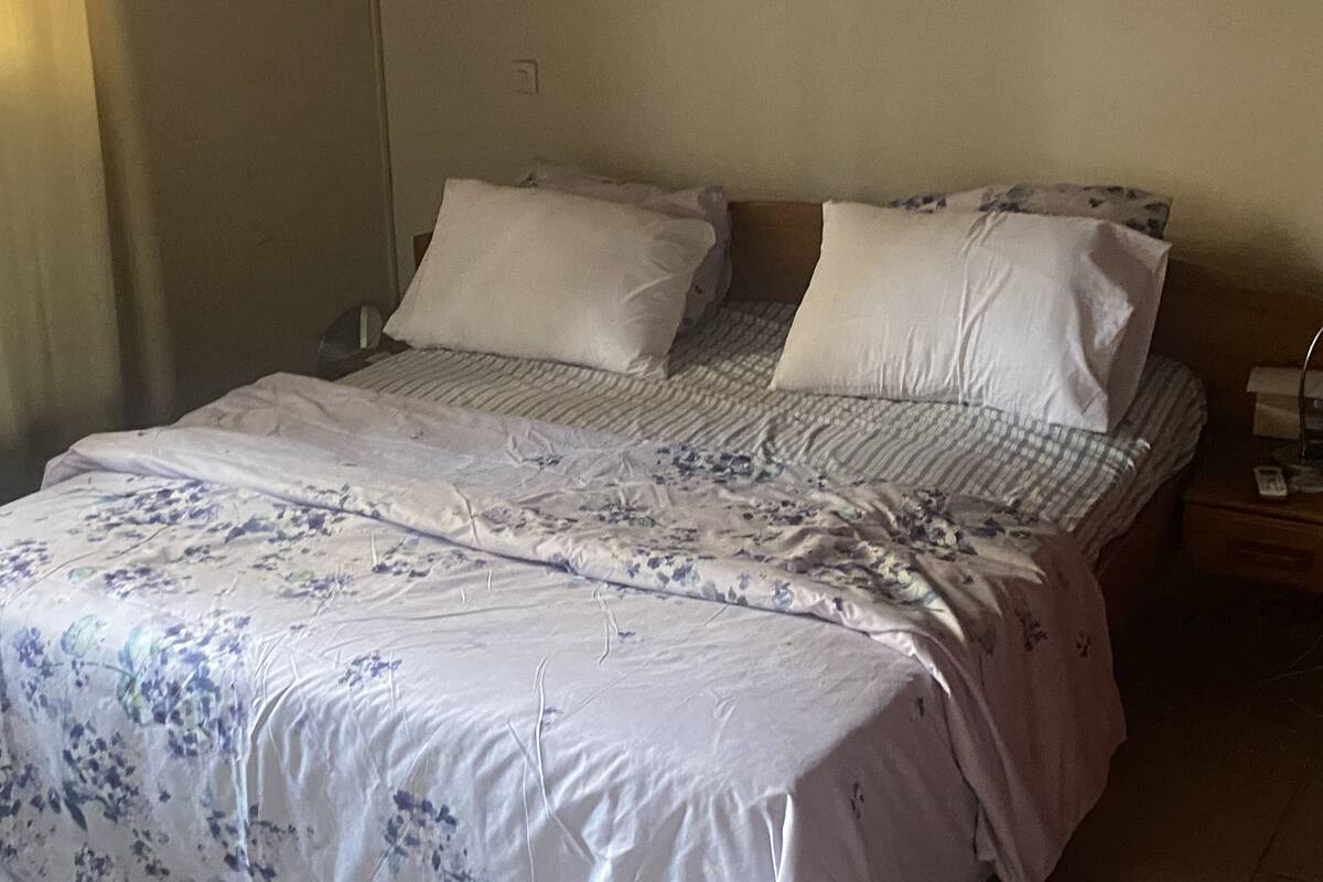 A bed with floral bedding, two pillows, and a bedside table with a lamp.