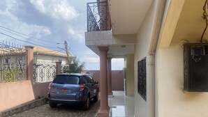 A narrow alleyway with a parked car, a gated entrance, and a building with a tiled floor and a balcony. - Manoir des Princesses Ekoumdoum (Yaoundé)