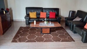 A living room with a brown patterned rug, two black leather sofas with colorful cushions, a wooden coffee table, and a small side table. - Manoir des Princesses Ekoumdoum (Yaoundé)
