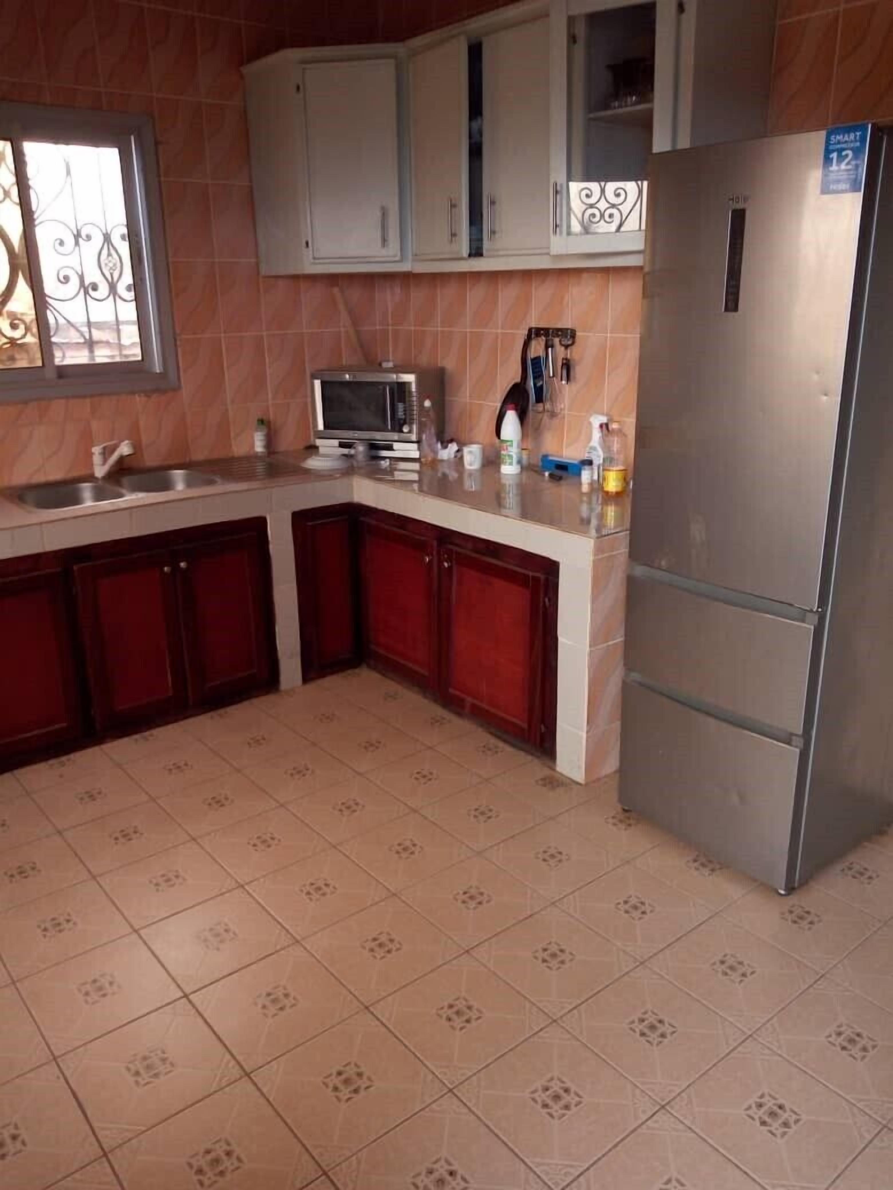 A kitchen with a stainless steel refrigerator, a microwave, and a sink. There are cabinets above the counter and a window with decorative ironwork.