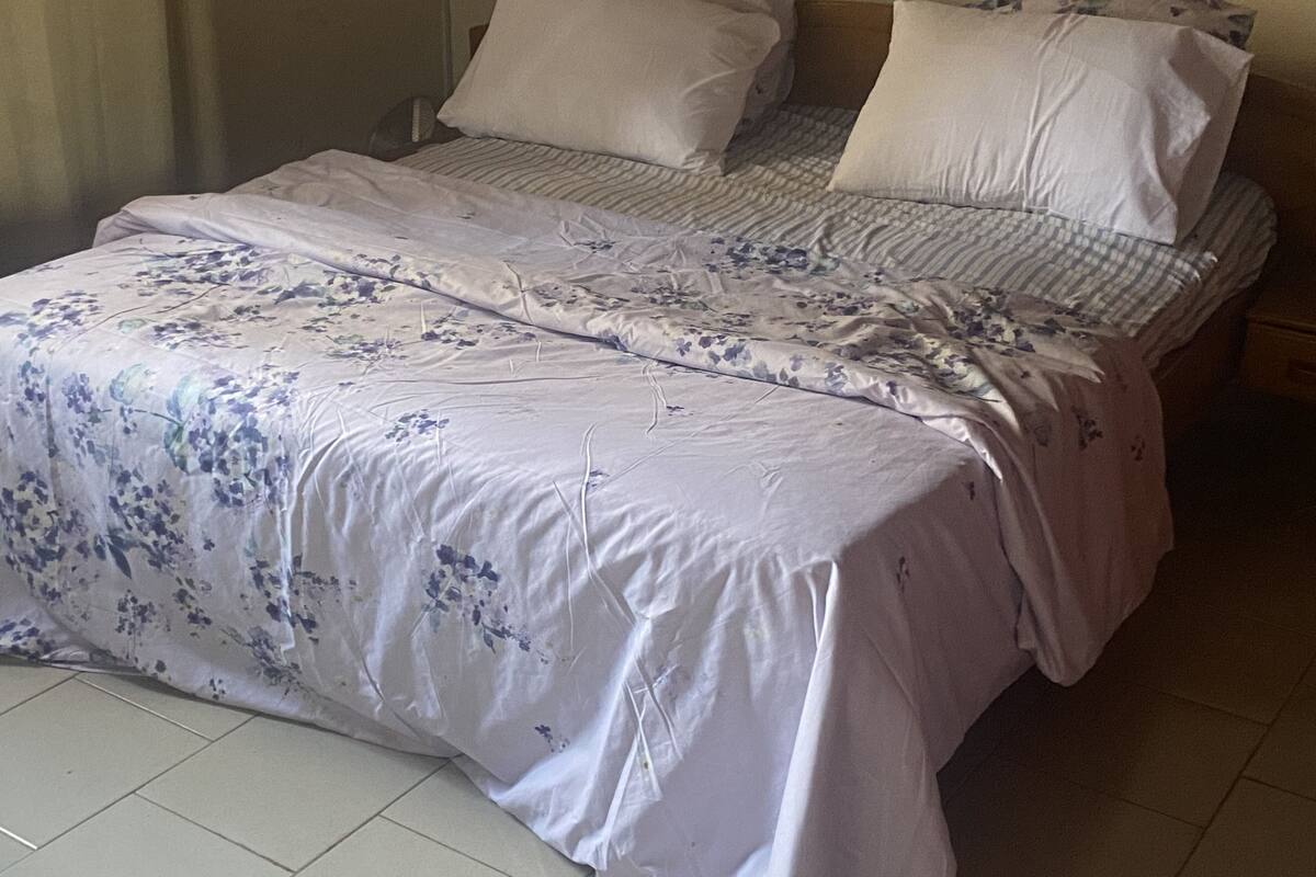 A neatly made bed with floral bedding and pillows, a bedside table, and a plain wall.