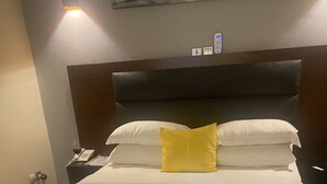 A hotel room with a bed, a bedside table with a phone and a glass of wine, and a wall-mounted light fixture. - Manoir des Princesses Ekoumdoum (Yaoundé)
