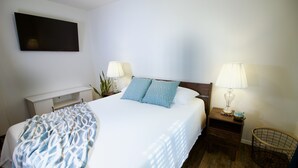 A neatly made bed with a patterned blanket, two bedside lamps, a small wooden nightstand, and a wall-mounted TV. - 3 blks to Historic downtown Courthouse & Whiskey Row. King bed. Dog Friendly (Prescott)